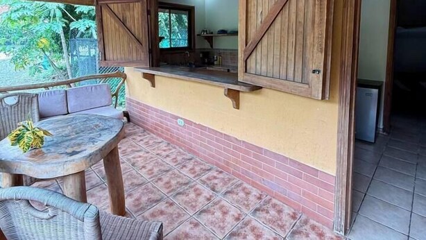 An outdoor patio with a wooden ceiling, a table with chairs, and a view of the kitchen through a window. - 2 bed, 2 bath, full kitchen. With pool & parking. (Puerto Viejo de Talamanca)