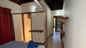 A narrow hallway with a bed on the left, a door at the end, and a small wooden shelf on the right. - 2 bed, 2 bath, full kitchen. With pool & parking. (Puerto Viejo de Talamanca)