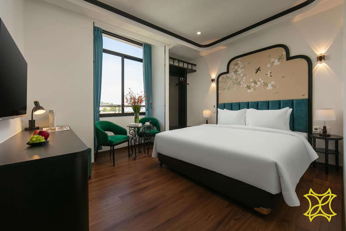 A hotel room with a large bed, a desk with a lamp, a chair, and a view of the outdoors.