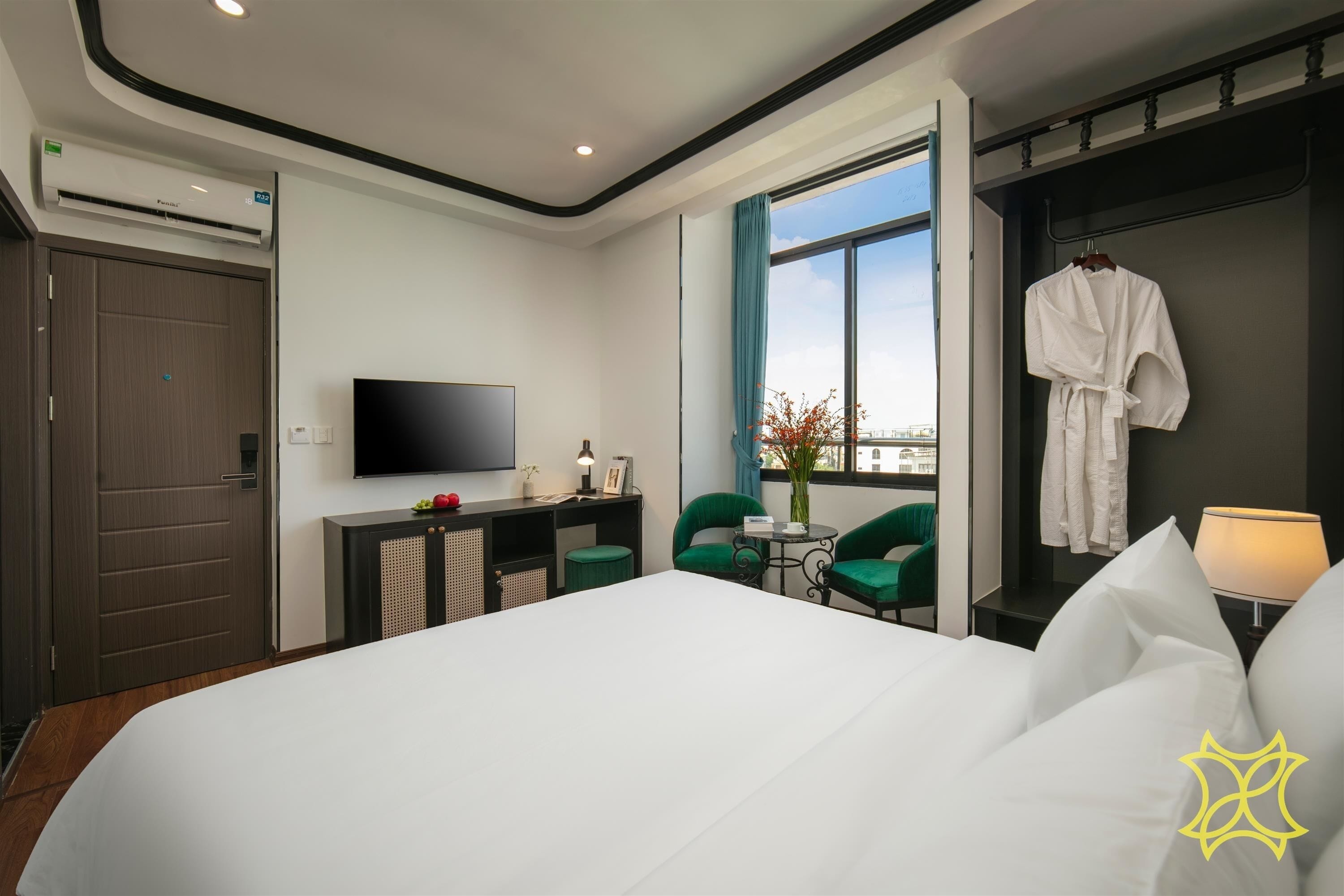 A hotel room with a large bed, a desk with a flat-screen TV, a seating area with chairs, a robe hanging on the wall, and a window with a view.