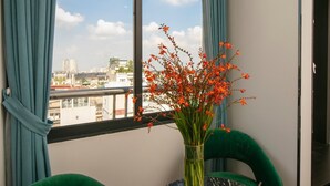 Una habitación con vistas a la ciudad, una mesa con un florero y sillas verdes.
