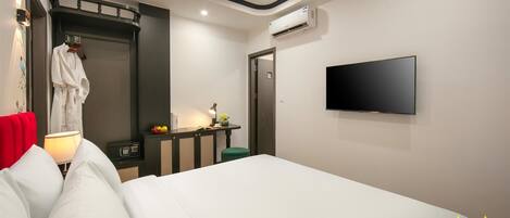 Una habitación de hotel moderna con una cama grande, un televisor de pantalla plana en la pared, una mesita de noche con lámpara, un taburete verde pequeño y una bata colgada en un perchero.
