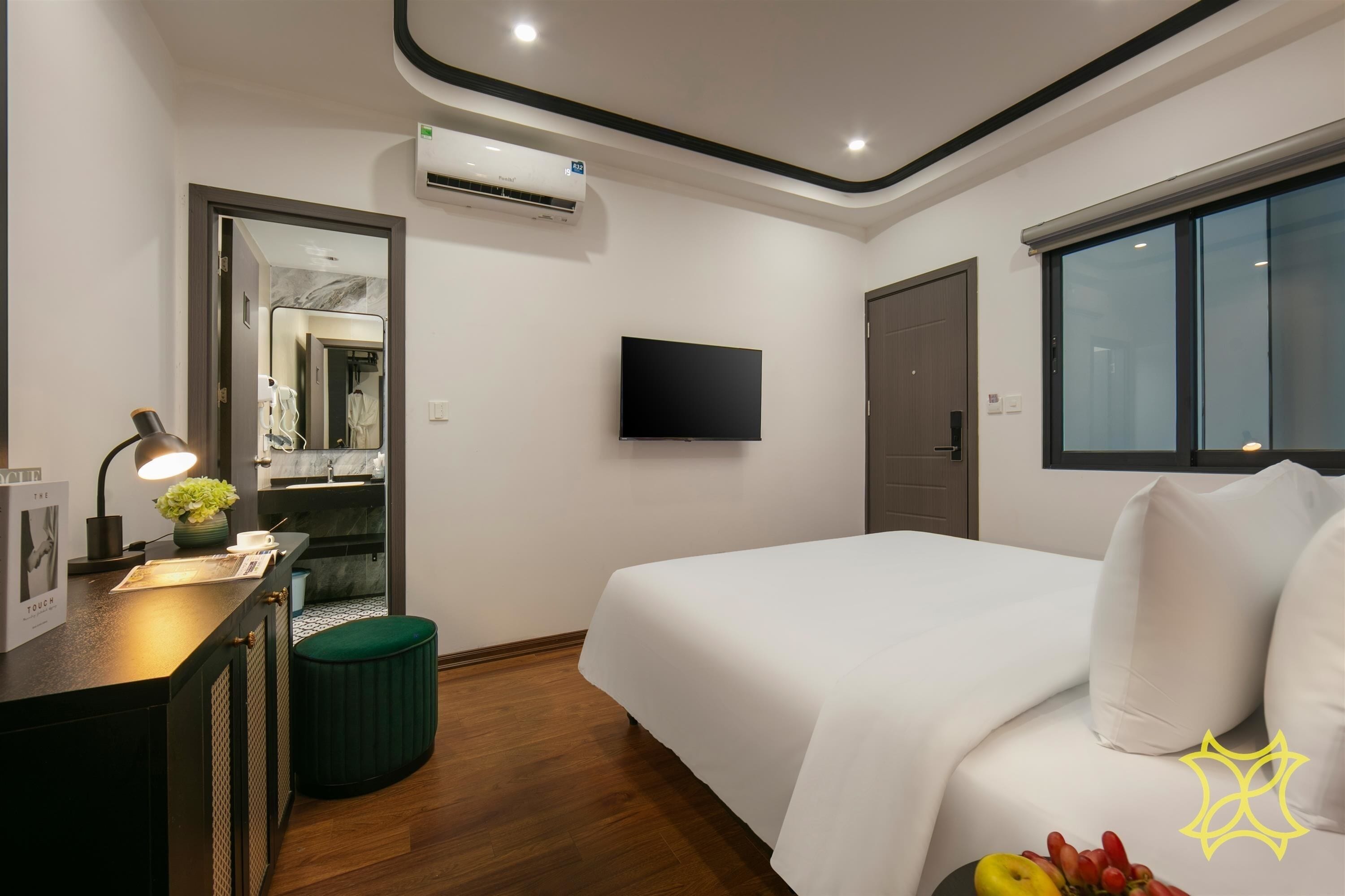 A modern hotel room with a bed, a desk with a lamp, a mirror, and a TV.