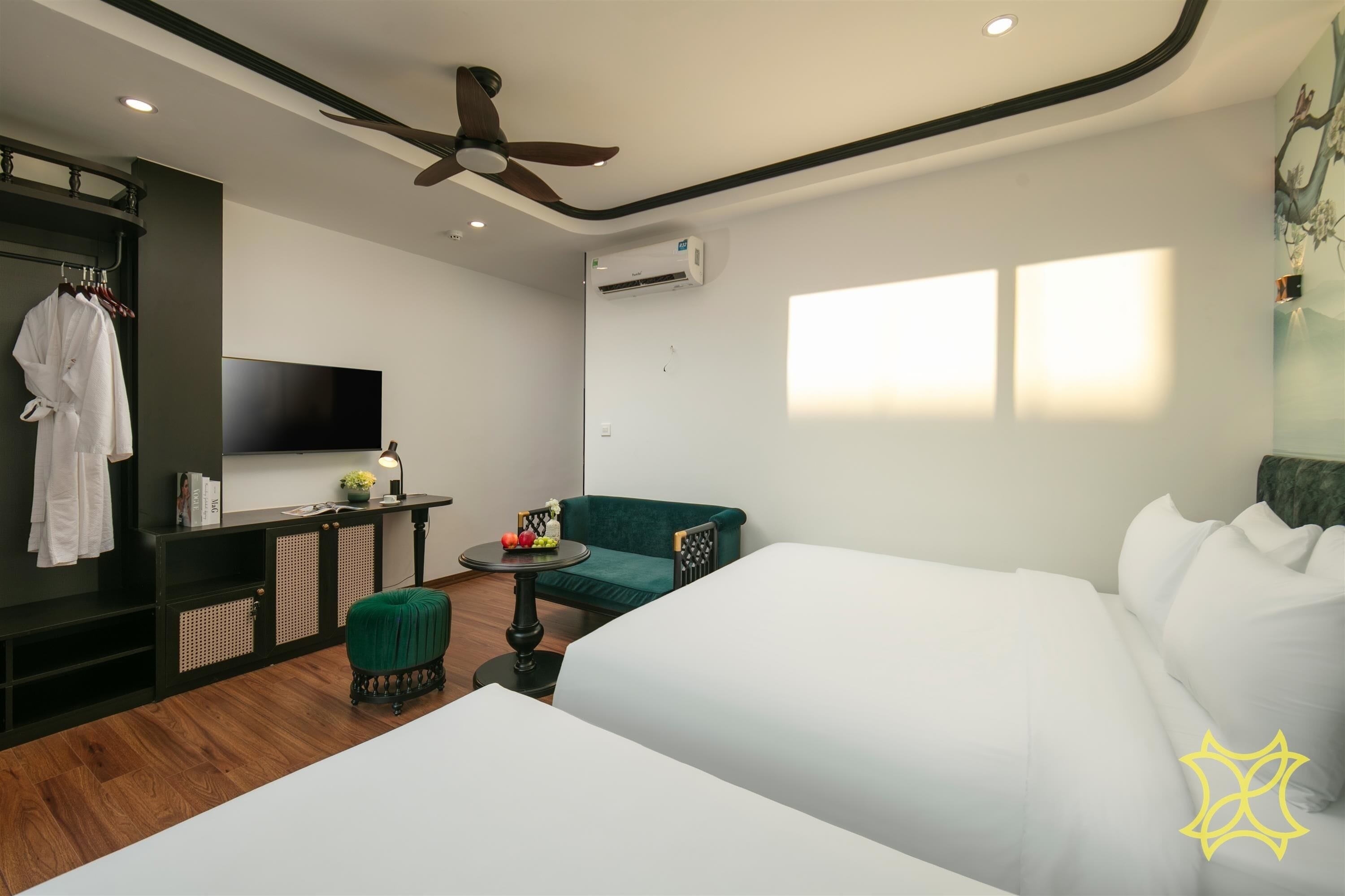 A hotel room with a bed, a green sofa, a small round table with fruit, a TV, and an air conditioning unit.