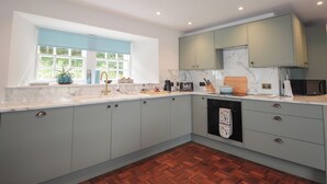 A modern kitchen with light blue cabinets, a marble countertop, and a wooden floor. - Srondubh (Achnasheen)