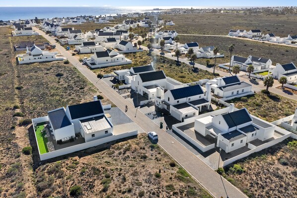 An aerial view of a residential area with white houses, a road, and a clear view of the ocean.