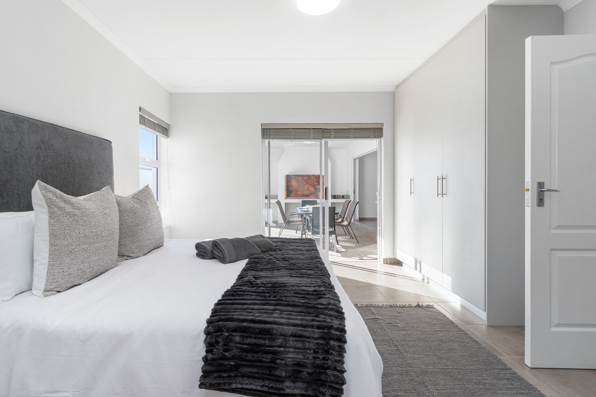 A modern bedroom with a large bed, a black fur throw, and a view into a dining area.