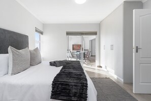 Un dormitorio moderno con una cama grande, un plaid de piel sintética y vista a un comedor.