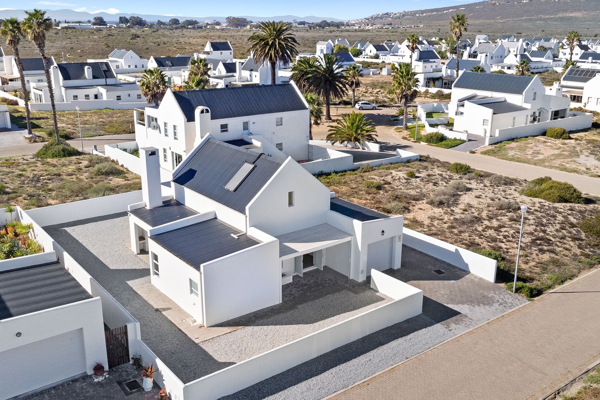 A modern residential area with white houses, some with solar panels, and a few palm trees.