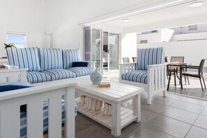 Una sala de estar moderna con sofás azul y blanco a rayas, una mesa de centro blanca y un comedor con mesa y sillas.