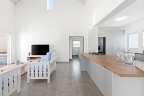 Una habitación moderna y bien iluminada con una mesa de comedor de madera, un sofá blanco y un televisor en una esquina.