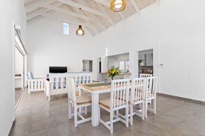 Una habitación amplia con techo alto, paredes blancas y una mesa de comedor de madera con sillas blancas.
