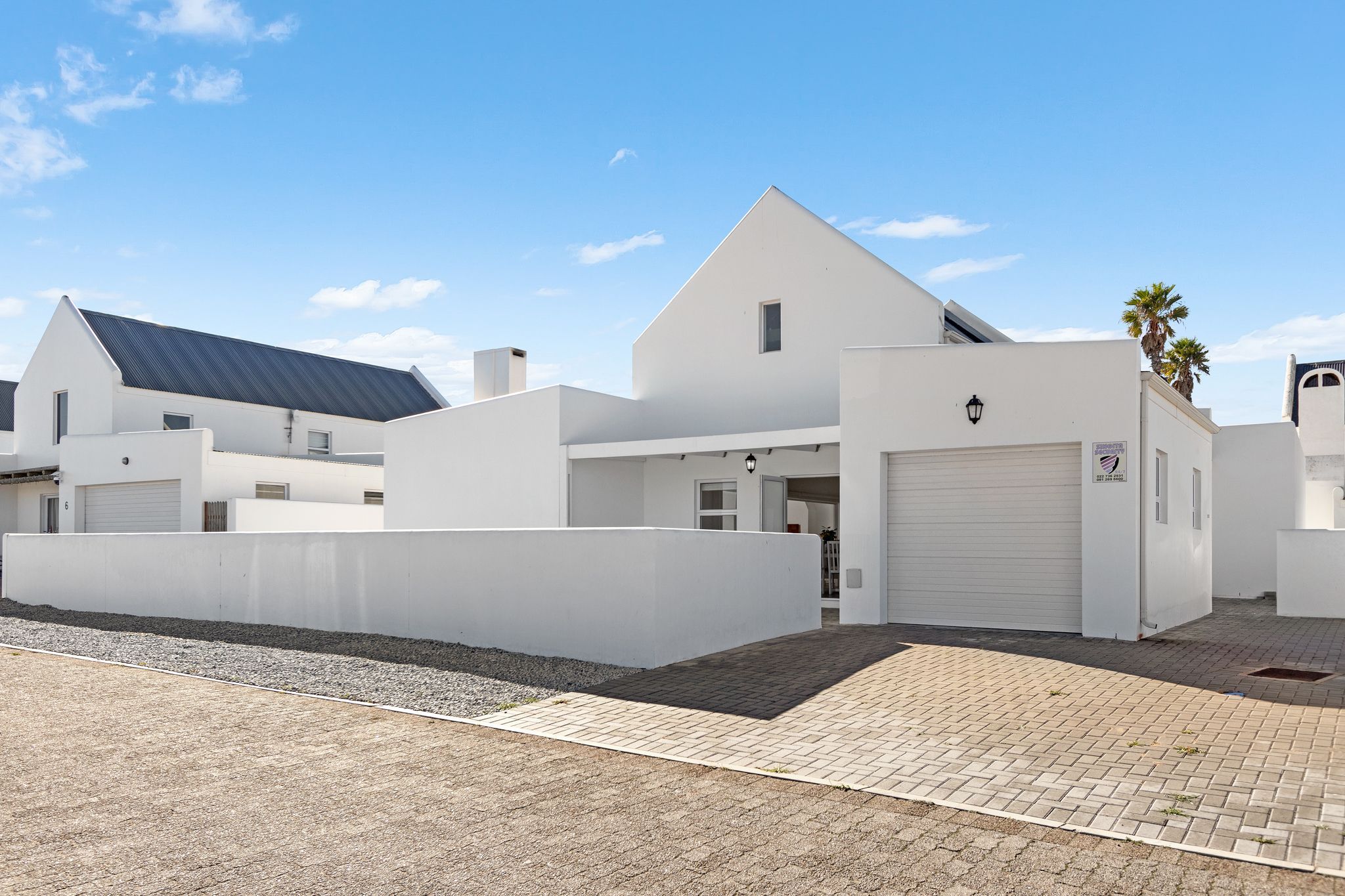 En moderne hvid bygning med garage, solpaneler og en asfalteret indkørsel.