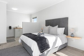 Un dormitorio moderno con una cama grande, una mesita de noche con lámpara y vistas al baño.