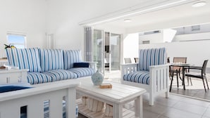 Un salon moderne avec des canapés bleus et blancs à rayures, une table basse blanche et un coin repas comprenant une table et des chaises.