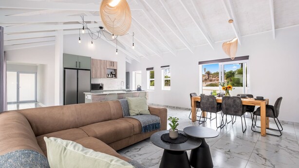 A spacious living area with a large brown sofa, a dining table with chairs, and a kitchen in the background. - Sunlit Oasis Ocean and Golf Retreat (St. Helena Bay)