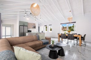 Un salón amplio con un sofá marrón grande, una mesa de comedor con sillas, y una cocina al fondo.