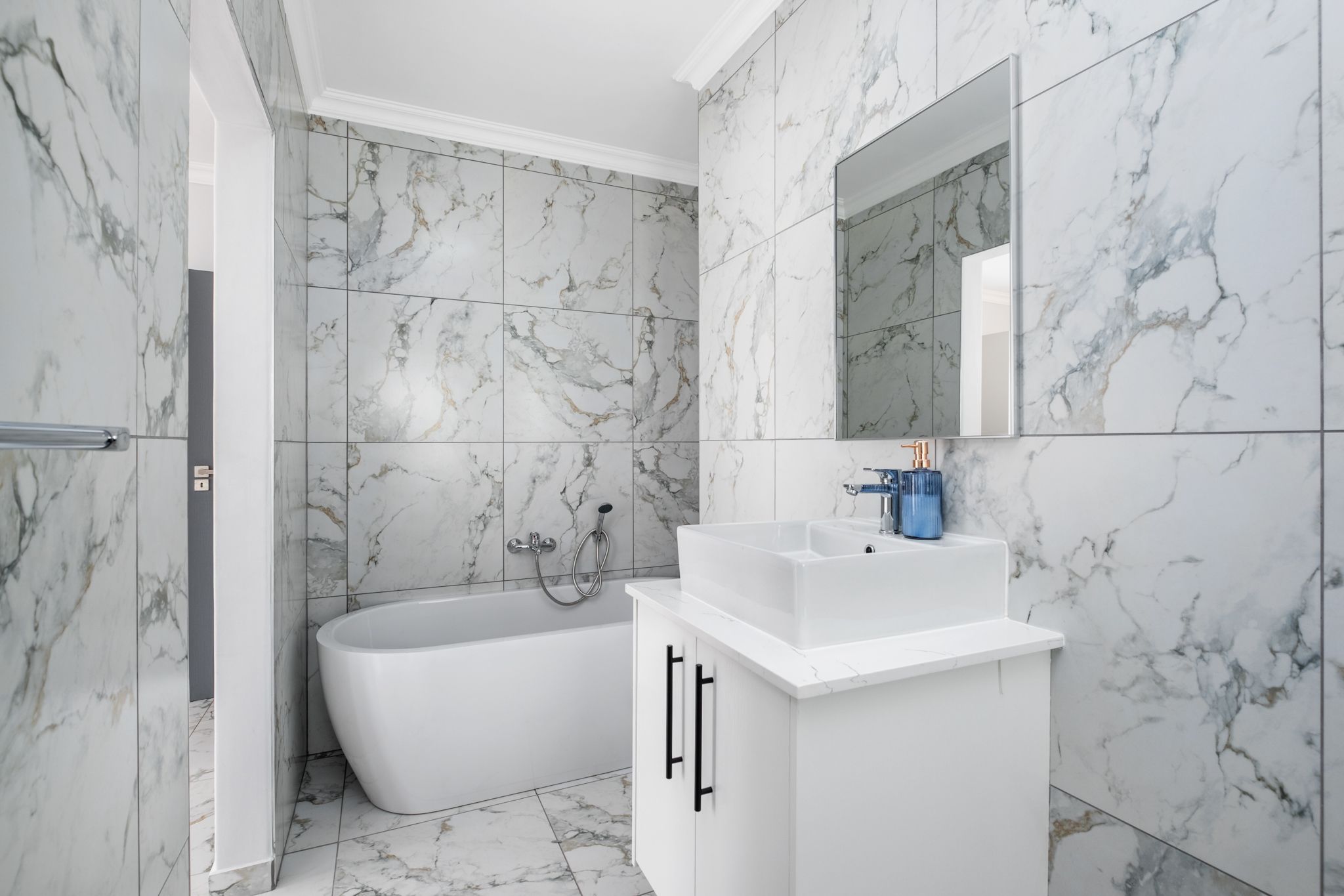 A modern bathroom with marble tiles, a freestanding bathtub, and a white vanity with a mirror.