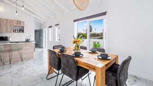 A modern kitchen with wooden cabinets, a marble countertop, and a dining area with a wooden table and chairs. - Sunlit Oasis Ocean and Golf Retreat (St. Helena Bay)