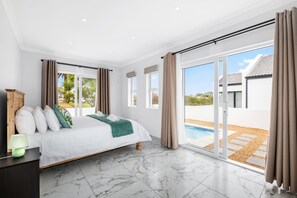 Un dormitorio con una cama grande, una mesita de noche, una lámpara y vistas a una piscina a través de una puerta corrediza de vidrio.