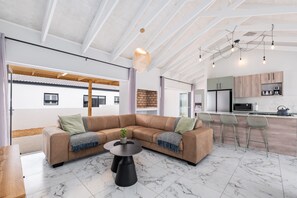 Una sala de estar moderna con un sofá seccional, una mesa de centro y una zona de cocina con taburetes de bar.