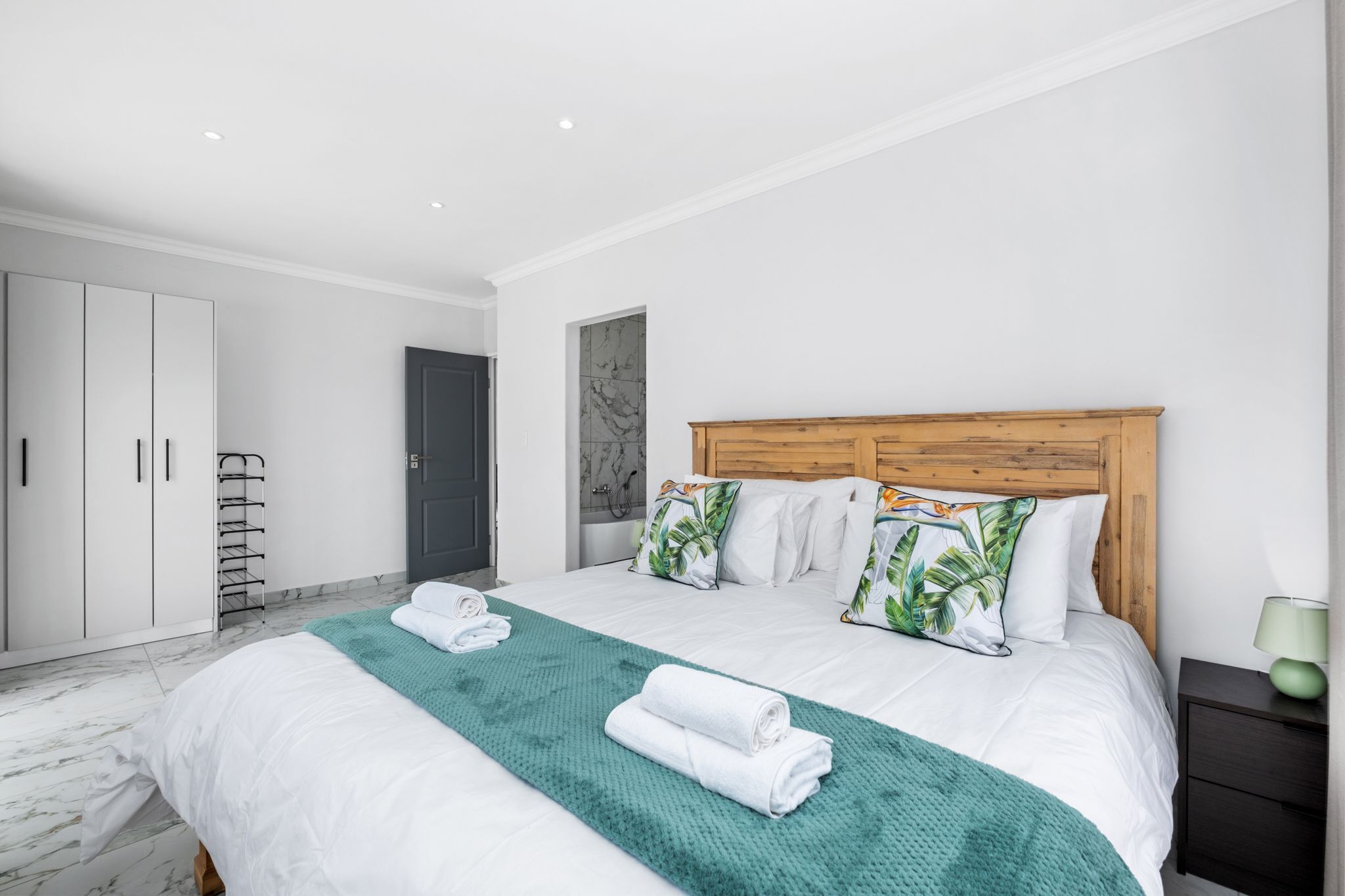 A modern bedroom with a large bed, white bedding, a wooden headboard, and a green throw blanket.