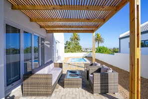 Un patio techado al aire libre con mobiliario de mimbre, una piscina y vistas del paisaje circundante.