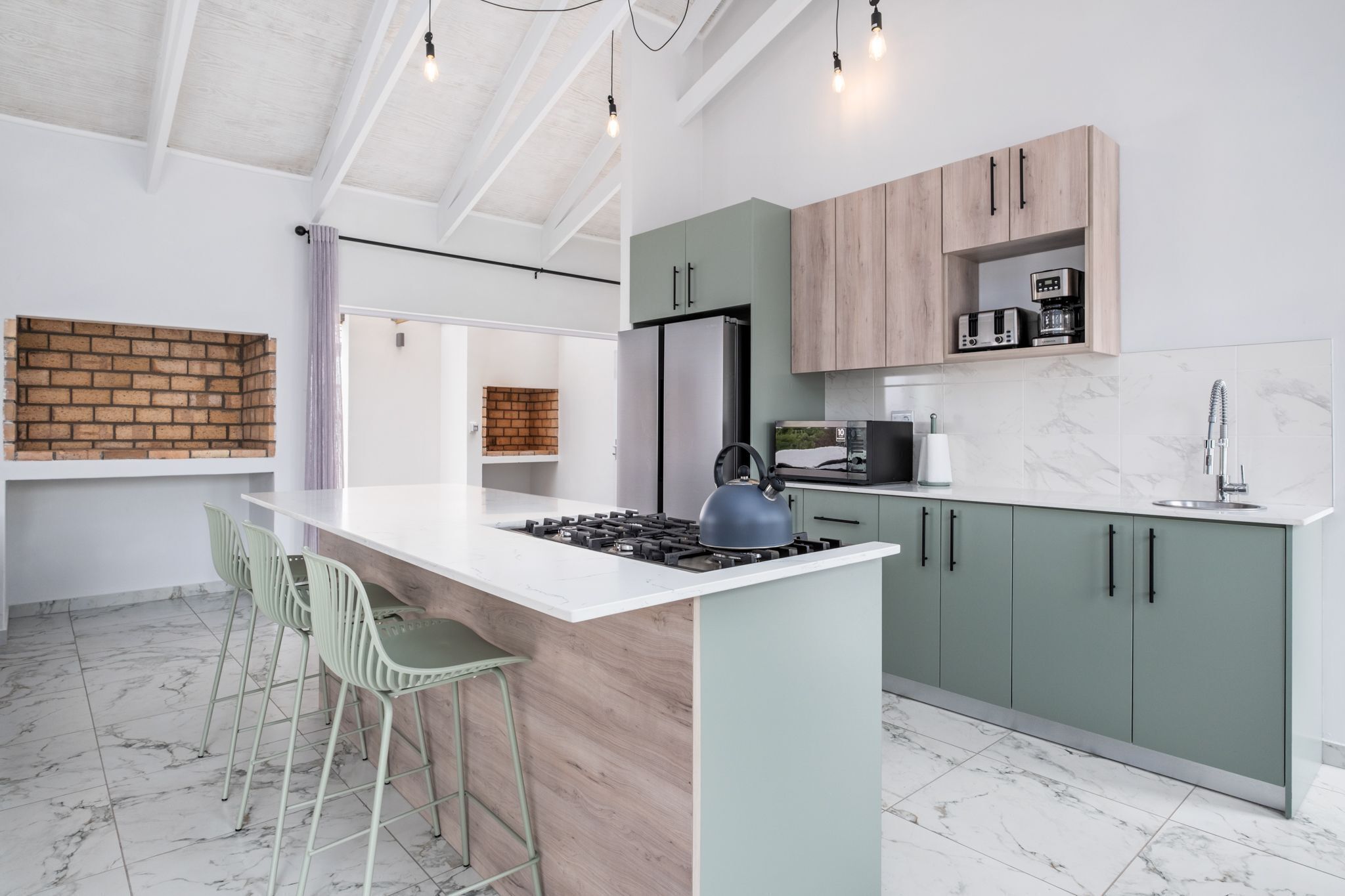A modern kitchen with a central island, green bar stools, and a brick accent wall.