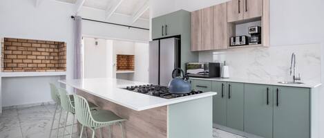 A modern kitchen with a central island, green bar stools, and a brick accent wall.