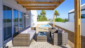 A covered outdoor patio with wicker furniture, a pool, and a view of the surrounding landscape. - Sunlit Oasis Ocean and Golf Retreat (St. Helena Bay)