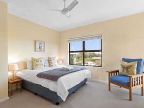A bedroom with a bed, a chair, a nightstand, a ceiling fan, and a window with a view of the outside. - Par Excellence Villa (Langebaan)
