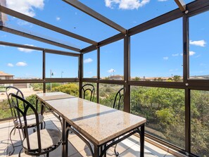 Una habitación iluminada por el sol, con una mesa y sillas, grandes ventanas que ofrecen vistas a zonas verdes y edificios lejanos.