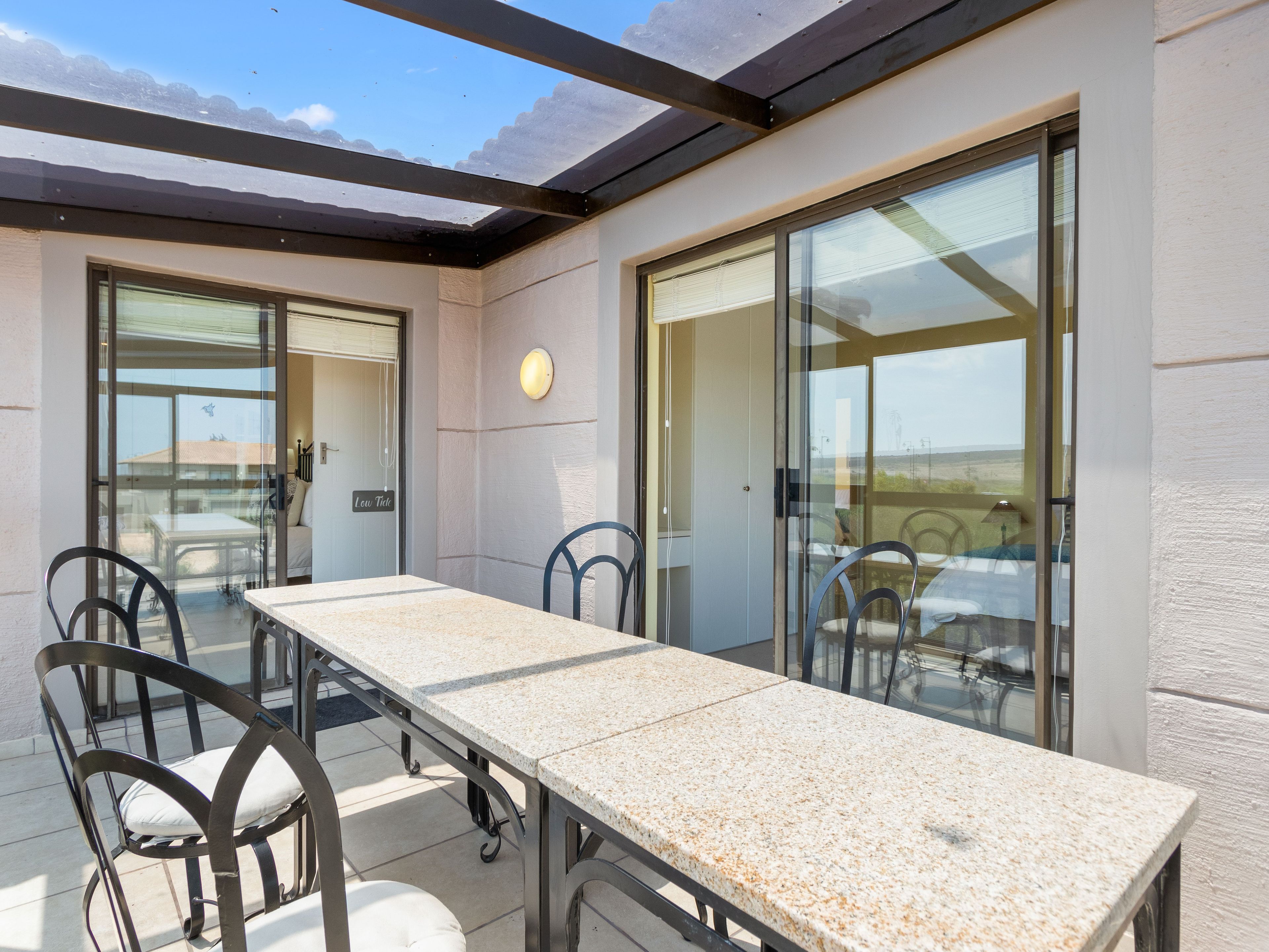 A covered outdoor dining area with a table and chairs, large sliding glass doors, and a view of the landscape.