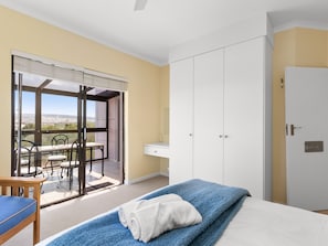 A bedroom with a bed, a desk, a chair, and a view of the outdoors.