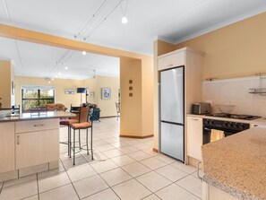 A modern kitchen with a refrigerator, stove, and bar stools. - Par Excellence Villa (Langebaan)