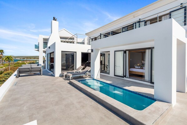 Une maison moderne à deux étages, dotée d’une piscine, d’un espace extérieur aménagé et offrant une vue sur la mer.