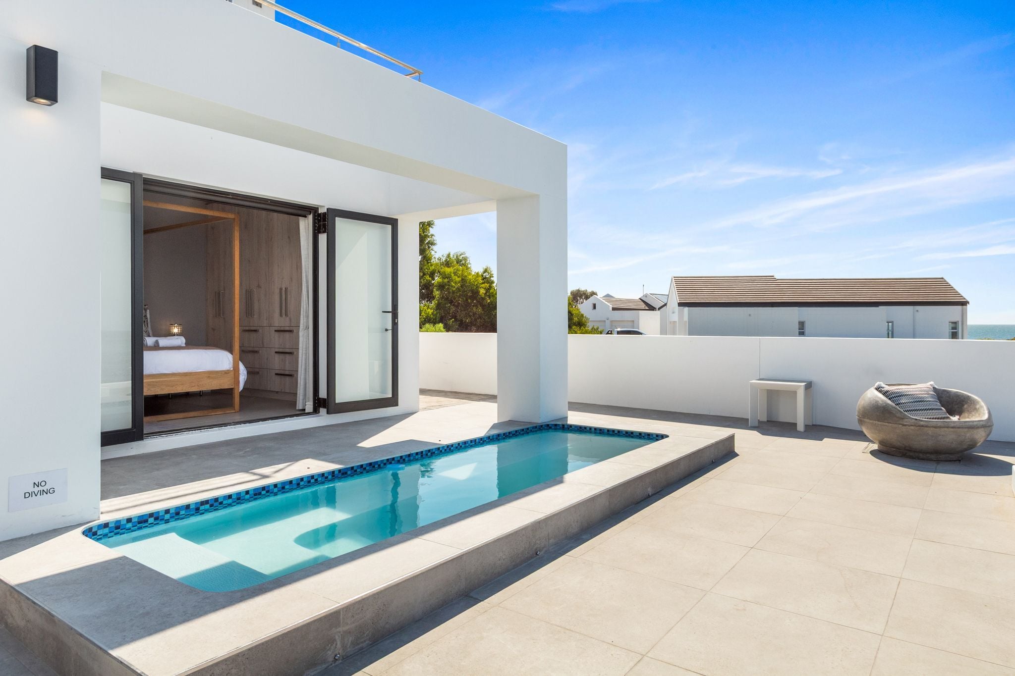 A modern outdoor pool area with a glass-enclosed bedroom and a view of the sea.