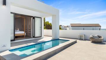 A modern outdoor pool area with a glass-enclosed bedroom and a view of the sea.