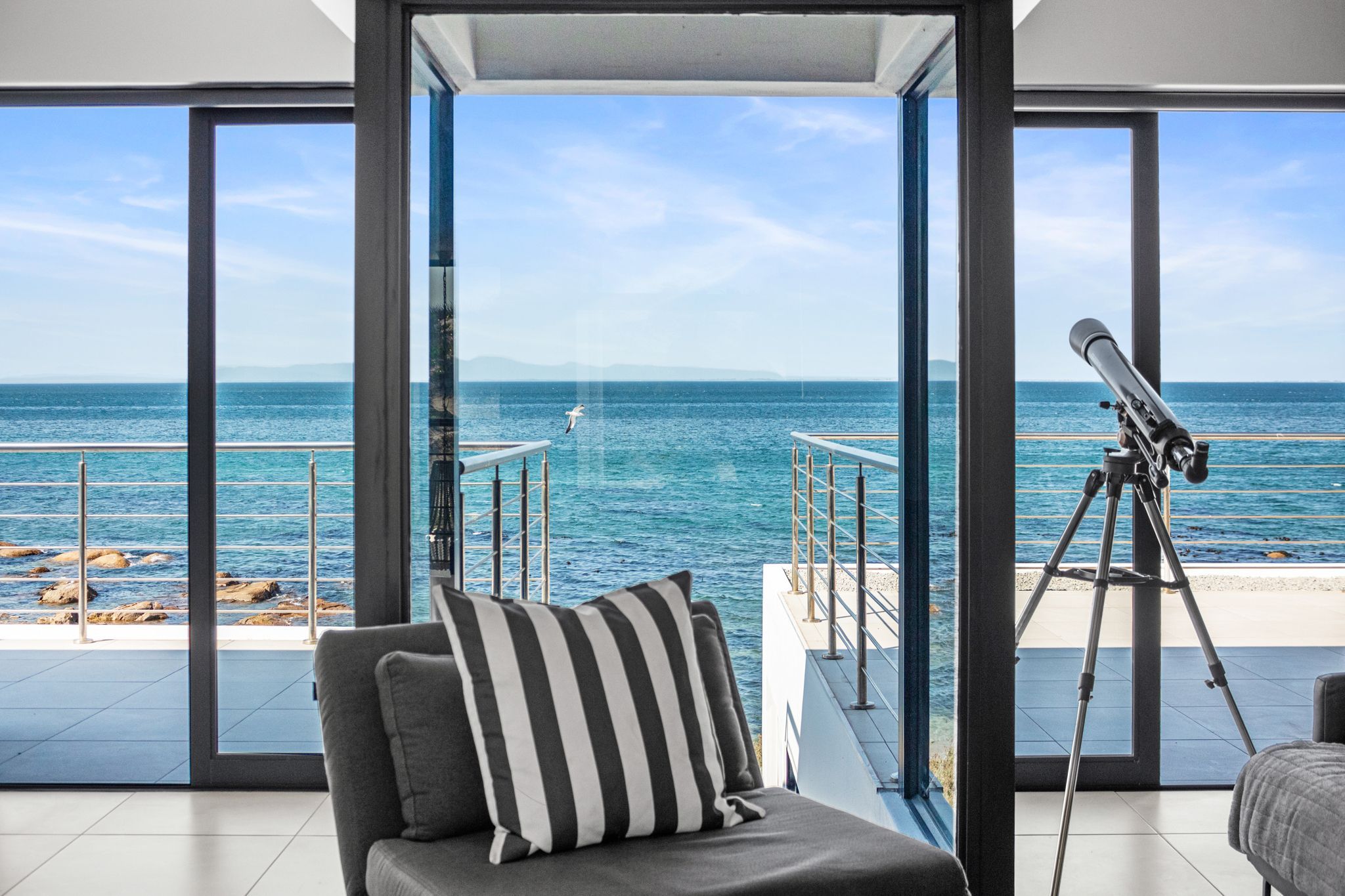 A balcony with a view of the sea, a telescope, and a striped pillow.