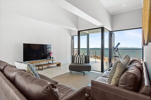 Una sala de estar moderna con un televisor de pantalla plana grande, sofás de cuero y un ventanal que da a un balcón con vistas al mar.