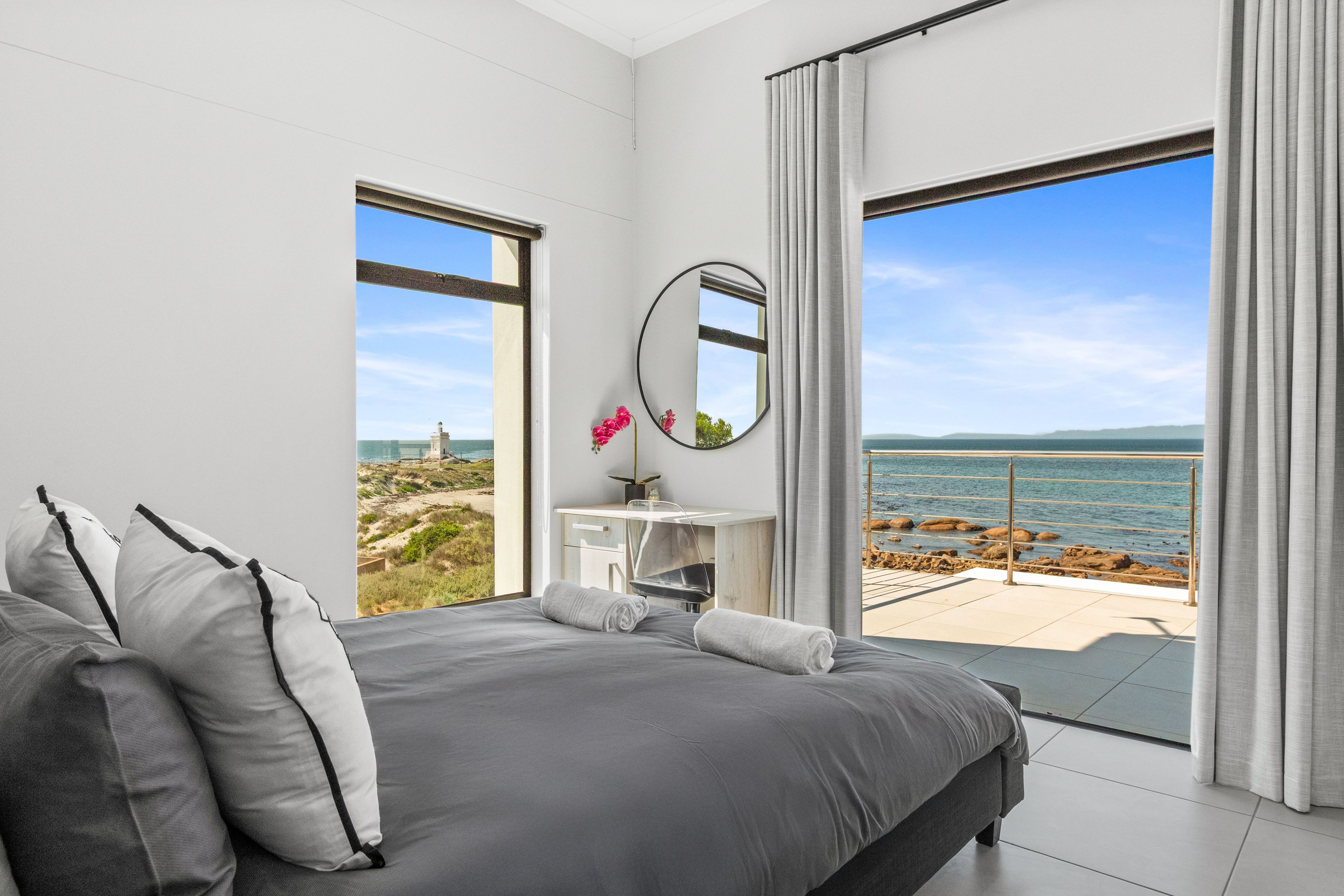 Un dormitorio moderno con una cama grande, un escritorio pequeño y vista al mar.