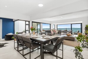 Un salon moderne avec un coin repas, de grandes fenêtres offrant une vue sur la mer et un espace salon confortable.