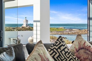 Une vue depuis une chambre dotée d’une grande fenêtre donnant sur une côte rocheuse, un phare et la mer.