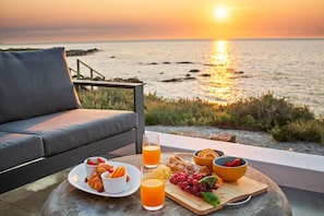 A seaside dining setup with a table, plates of food, and drinks, overlooking the ocean at sunset. - Shelley Point Beach Villa (St. Helena Bay)