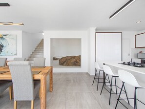 Egy modern konyha központi szigettel, fehér bárszékekkel és egy galériához vezető lépcsővel.