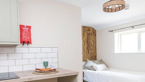 A compact room with a kitchenette, a bed with green bedding, and a wooden headboard.