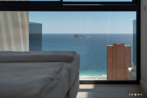 A bedroom with a large window overlooking the ocean and a tall building. - Torre Sakura By Leo Apartments (Benidorm)