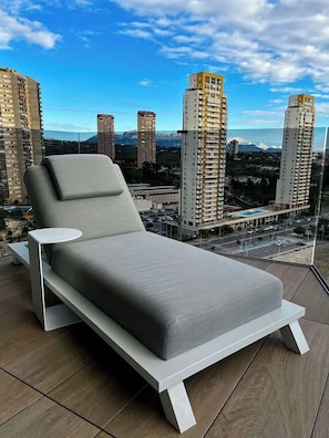 A modern lounge chair with a white frame and grey cushions, positioned on a balcony with a cityscape view. - Torre Sakura By Leo Apartments (Benidorm)