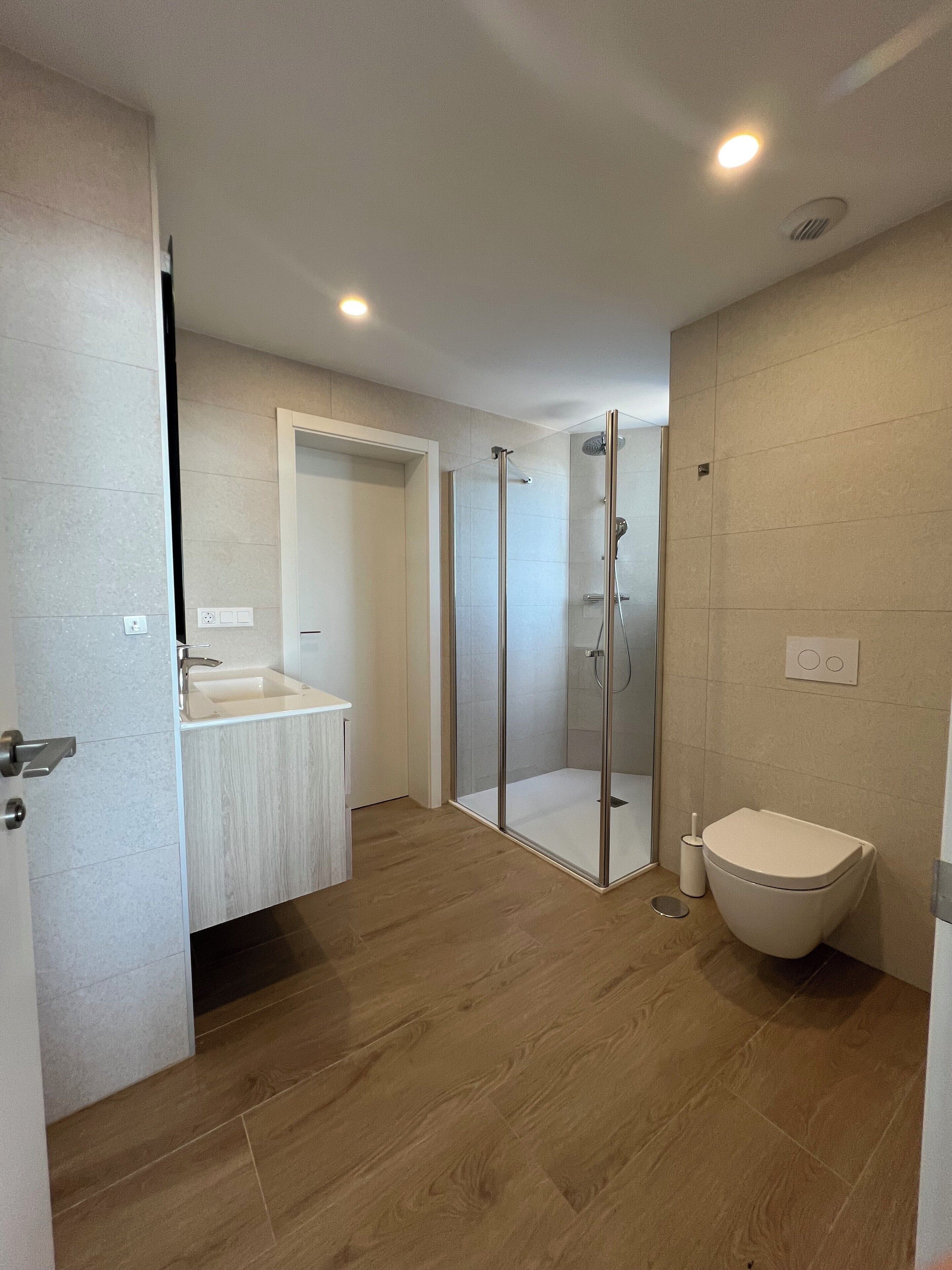 Ein modernes Badezimmer mit einer Duschkabine, einem Holzwaschtisch und einer Toilette.