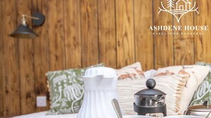 A wooden wall, a bed with pillows, a white vase, a black lantern, and two mugs with the Ashdene House logo. - Breeze Room 10 - Peaceful Single - New Forest (Dibden Purlieu)